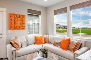 A modern living room with a beige sectional sofa, a round coffee table, and a large window offering a view of a residential area.