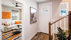 A hallway with a staircase, a door, a framed picture, and a sofa with cushions. - Iconic Big Sky Getaway | Epic Yellowstone Retreat! (Belgrade)