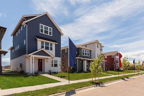 A residential area with modern two-story houses, a clear sky, and a well-maintained lawn.