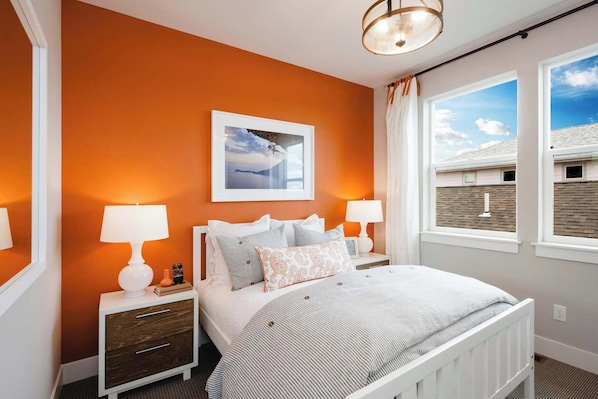 A bedroom with a bed, two bedside tables, a nightstand, a window with curtains, and a picture on the wall.