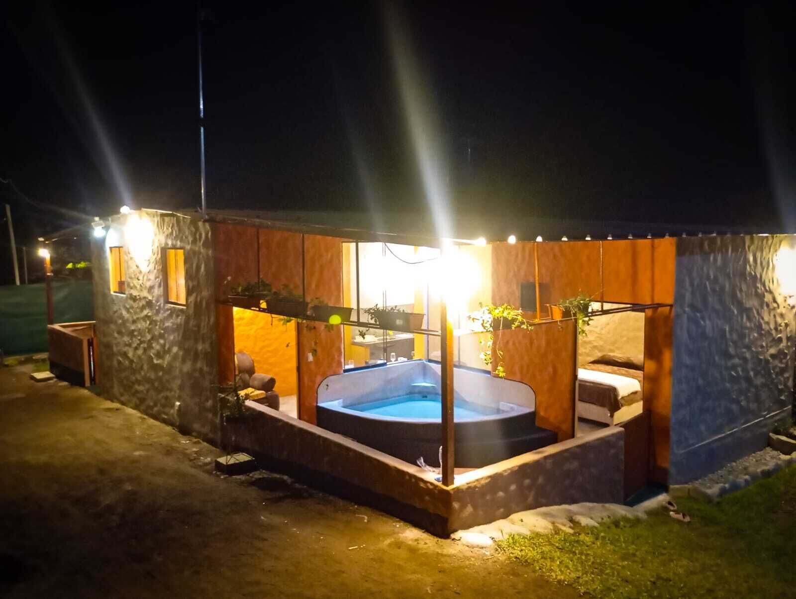 Un área de hidromasaje con revestimiento de piedra, rodeada por una terraza de madera e iluminada por luces exteriores.