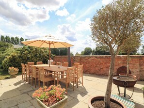 Eine Terrasse im Freien mit Tisch, Stühlen, einem Grill und Kübelpflanzen.