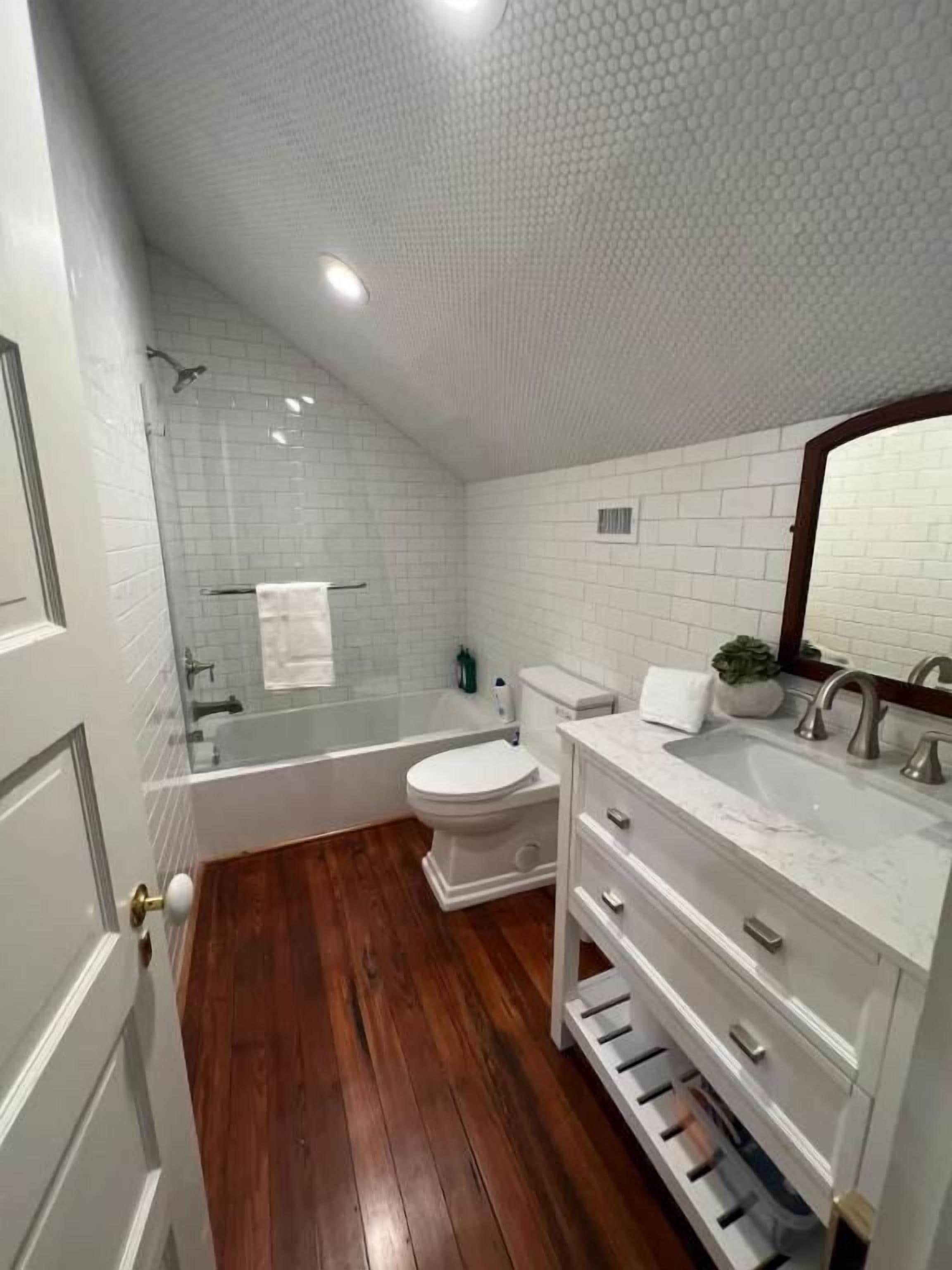 Ein Badezimmer mit Badewanne, Toilette und Waschbecken, mit weißen Fliesen und Holzböden.