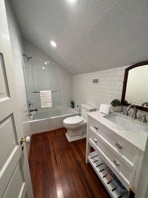 A bathroom with a bathtub, toilet, and sink, featuring white tiles and wooden flooring. - Rustic Luxury from Restoring Galveston (Galveston)