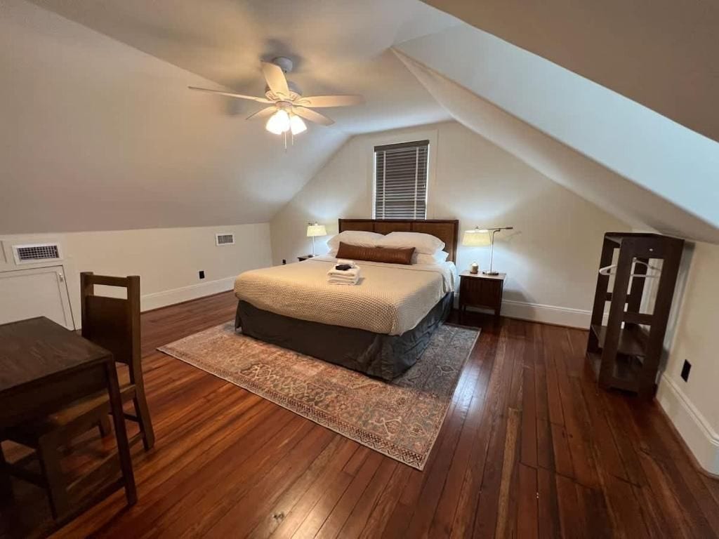 Een slaapkamer met een bed, bedlampen, een plafondventilator, een raam en een houten vloer.