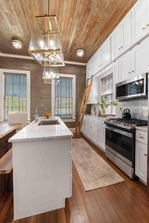 Una cocina con techo de madera, armarios blancos, una isla central y una estufa de acero inoxidable.
