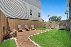 A backyard with a wooden fence, a lawn, and three Adirondack chairs. - Rustic Luxury from Restoring Galveston (Galveston)