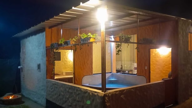 A hot tub under a wooden pergola with a stone wall and a fire pit outside.