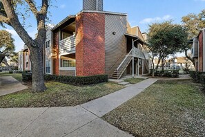 A modern two-story building with a brick facade and a covered outdoor staircase. - I114 – Private King Retreat | DFW 10 Min | Yard+W/D (Irving)
