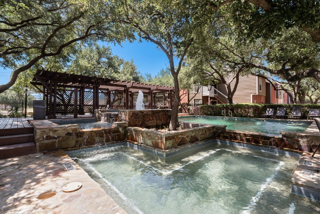 Area piscina con una pergola in legno, scalini in pietra e vista libera su un edificio sullo sfondo.
