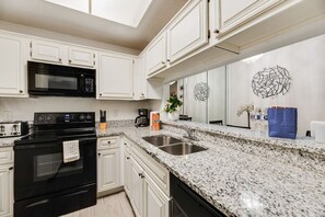 A modern kitchen with white cabinetry, a granite countertop, a black oven, a microwave, and a sink. - I114 – Private King Retreat | DFW 10 Min | Yard+W/D (Irving)