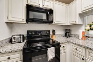 A kitchen with white cabinetry, a black microwave, a stove, a toaster, and a coffee maker. - I114 – Private King Retreat | DFW 10 Min | Yard+W/D (Irving)