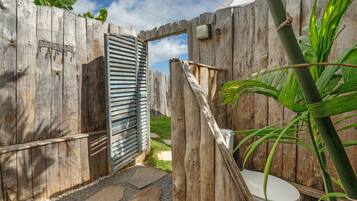 Un baño rústico al aire libre con valla de madera, portón metálico y asiento de inodoro.