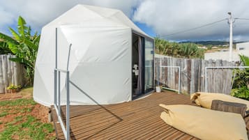 A tent-like structure with a door, a wooden deck, and a fence in a backyard setting.