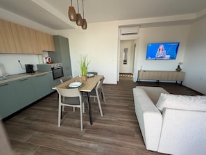 A modern living space with a dining area, kitchen, and a TV mounted on the wall. - Le Calendule Luxury Apartment (Olbia)