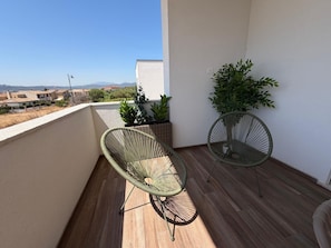 A balcony with two wicker chairs, a potted plant, and a view of distant buildings. - Le Calendule Luxury Apartment (Olbia)