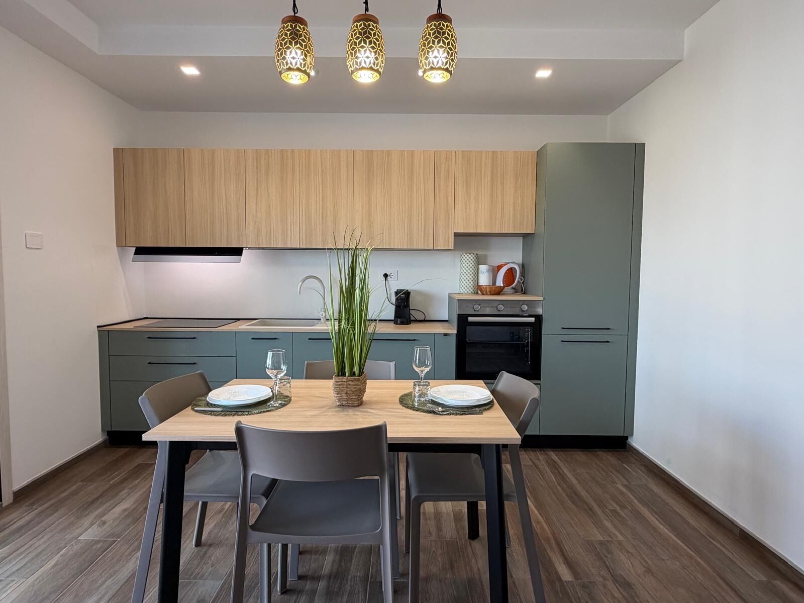 Una cocina moderna con gabinetes de madera, una mesa de comedor con sillas e iluminación colgante.