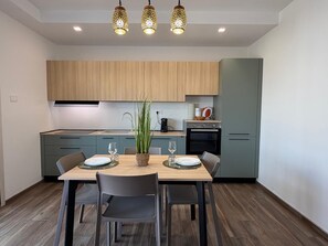 A modern kitchen with wooden cabinets, a dining table with chairs, and pendant lighting. - Le Calendule Luxury Apartment (Olbia)