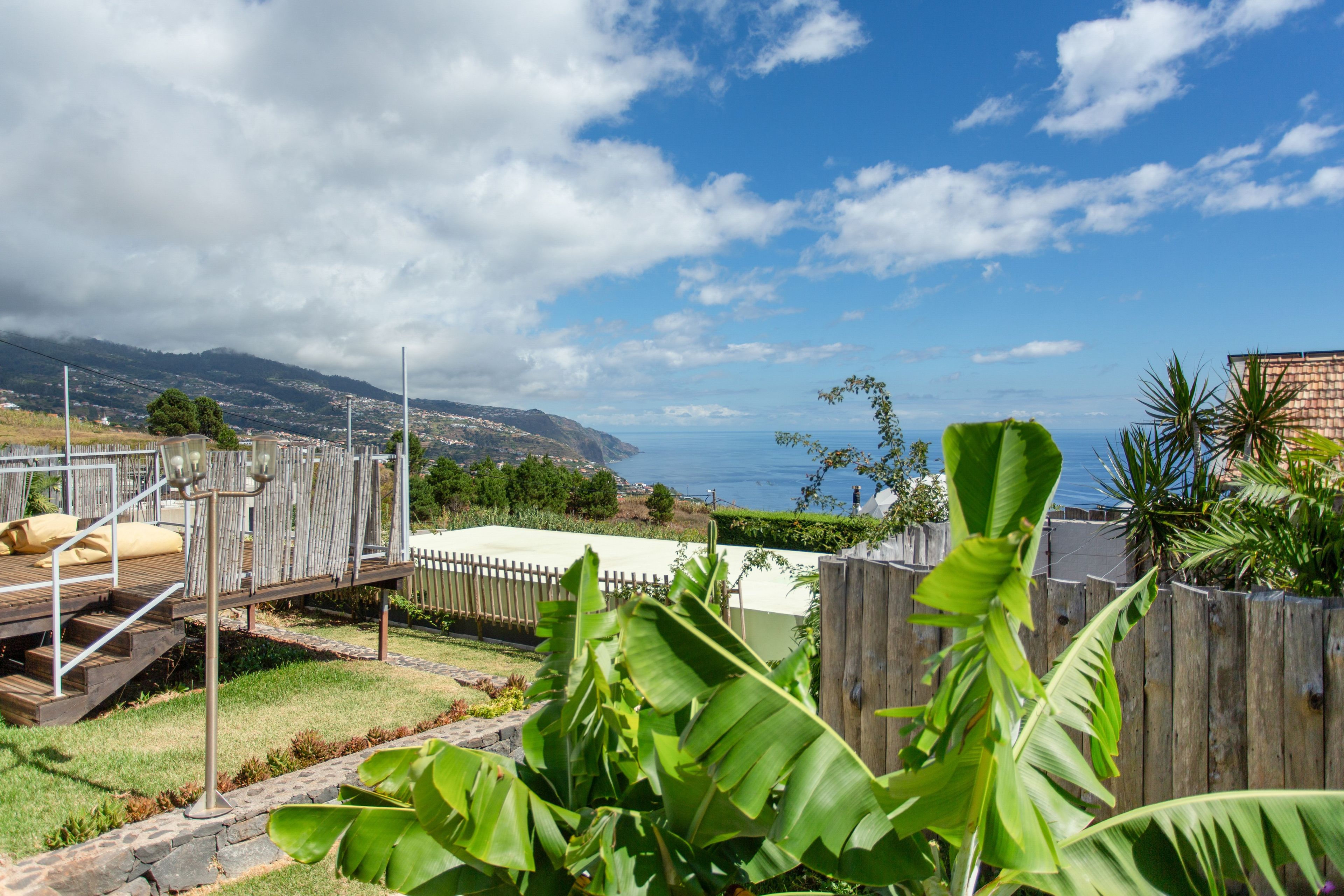 A backyard with a wooden deck, a white fence, and a view of the ocean and hills.