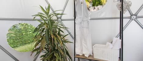 A room with a large potted plant, a white towel rack, and a shelf with towels and a basket.