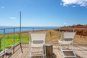 Una terraza con dos sillas blancas orientadas a una vista panorámica del océano y un paisaje con césped.
