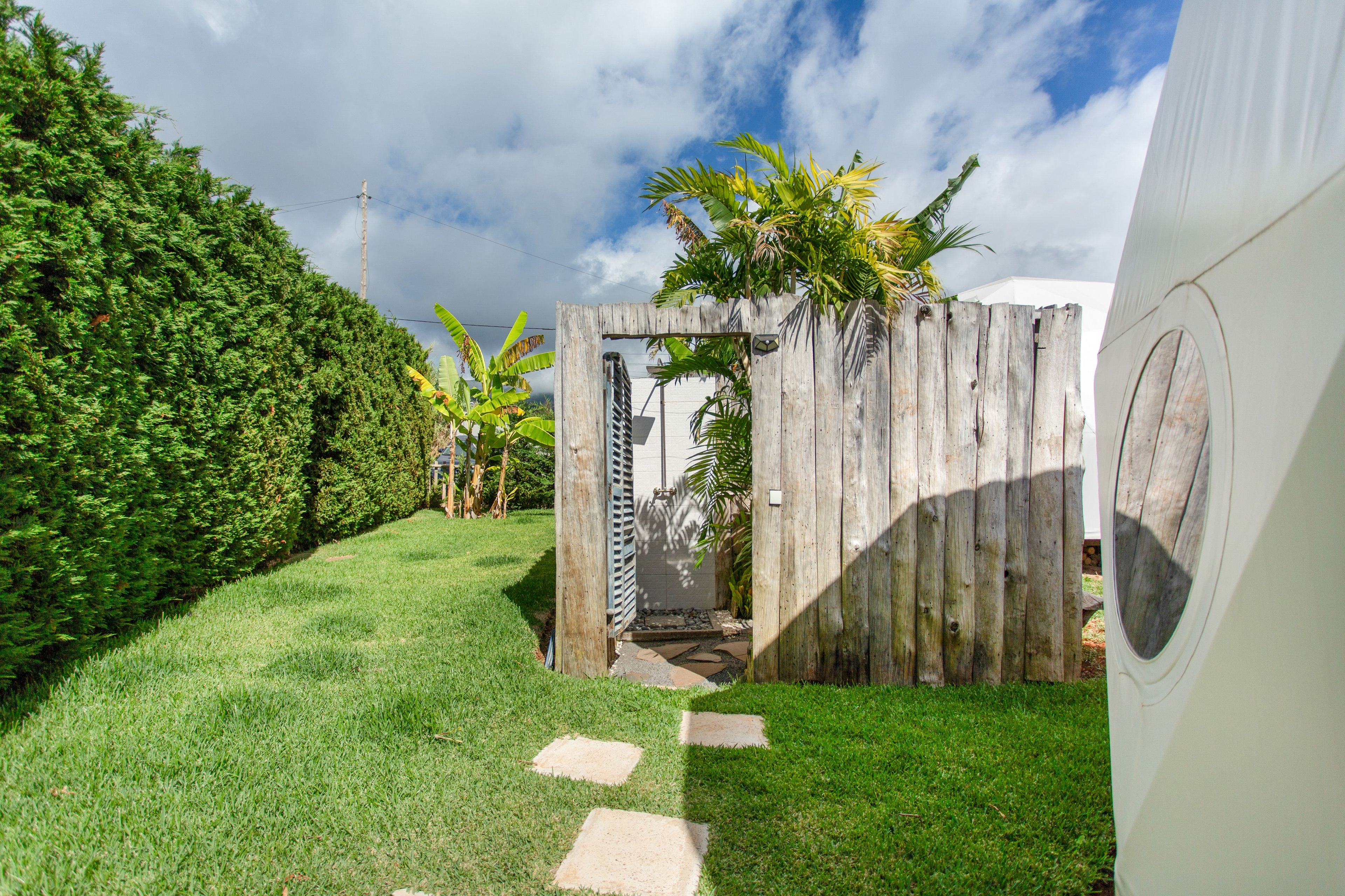 A pathway leading to a wooden gate with a metal gate, surrounded by a well-maintained lawn and a hedge.