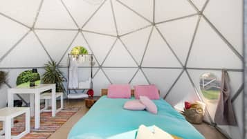 Eine Zelthütte mit einem Bett, Kissen, einem Hängesessel, einem Tisch und einer Pflanze.