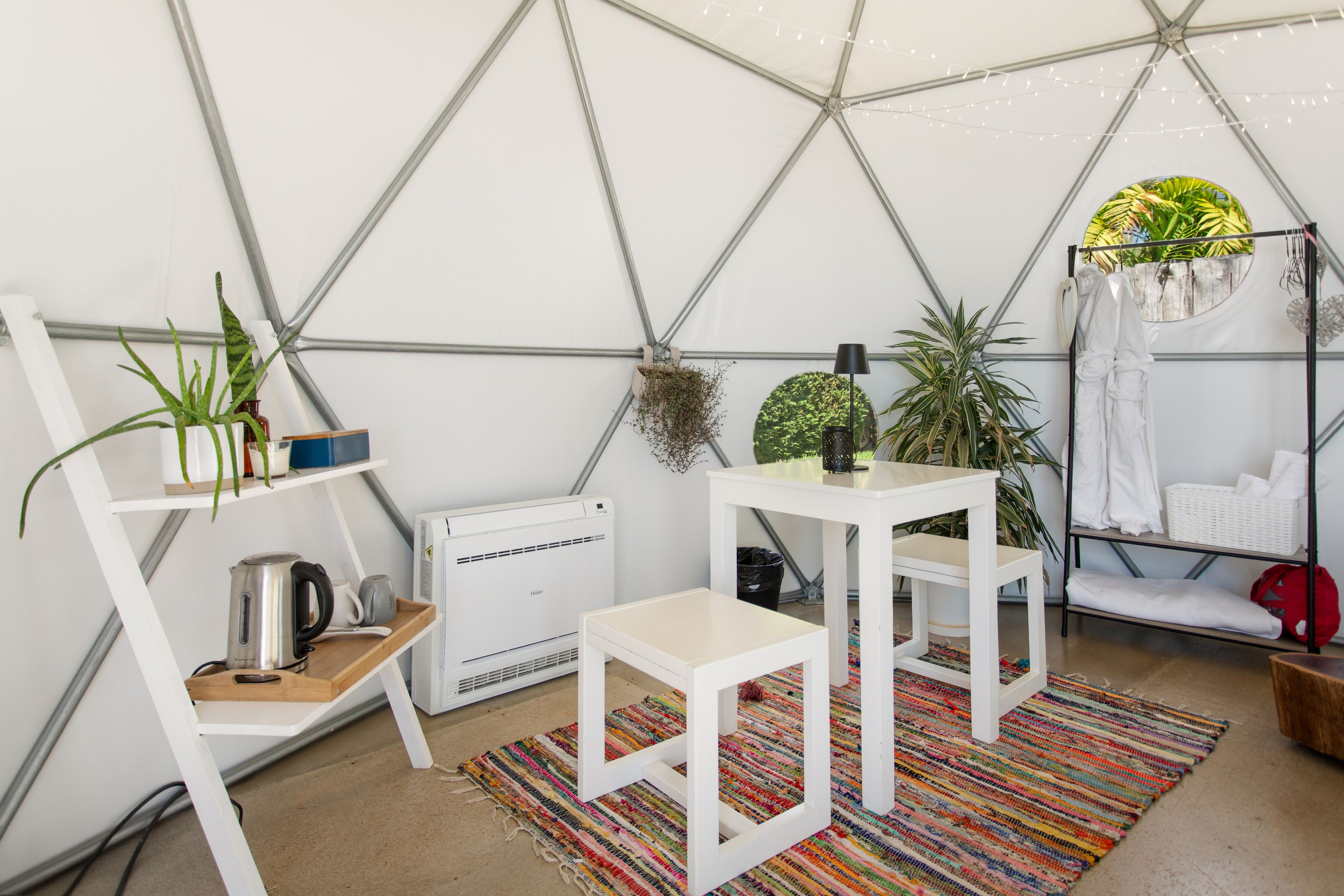Una habitación tipo tienda de campaña con muebles blancos, una alfombra colorida y varias plantas.