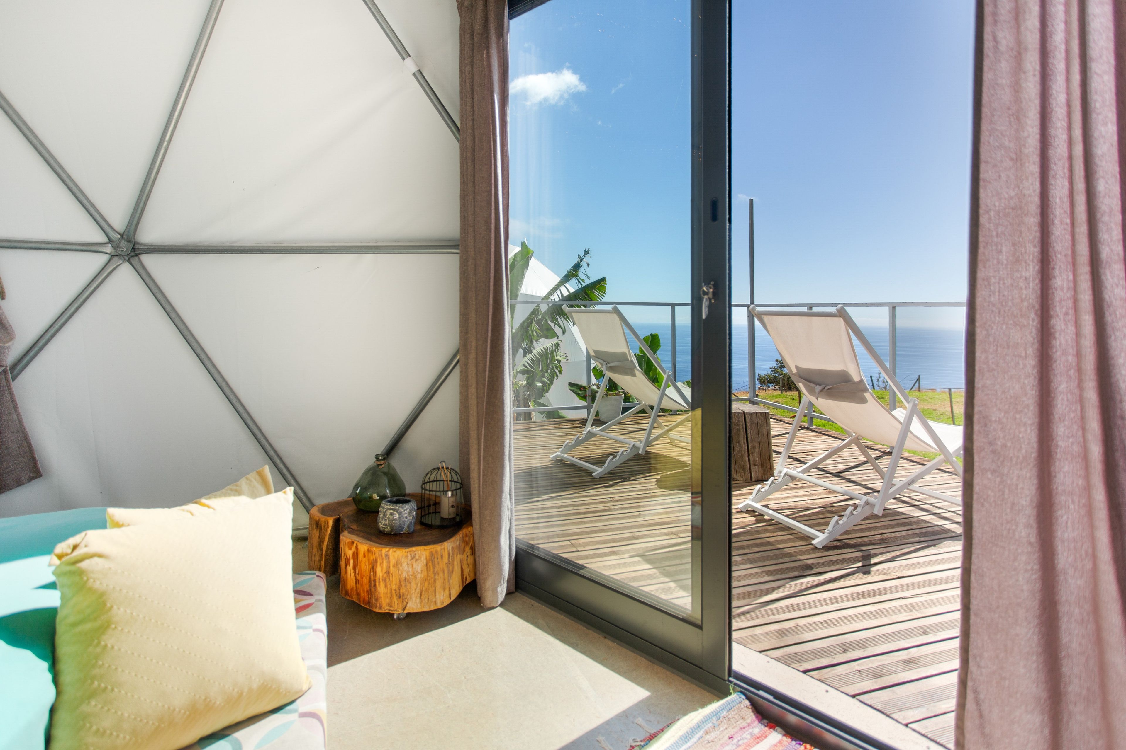 Un balcon avec vue sur la mer, une petite table d’appoint en bois agrémentée d’objets décoratifs et un lit avec un oreiller.