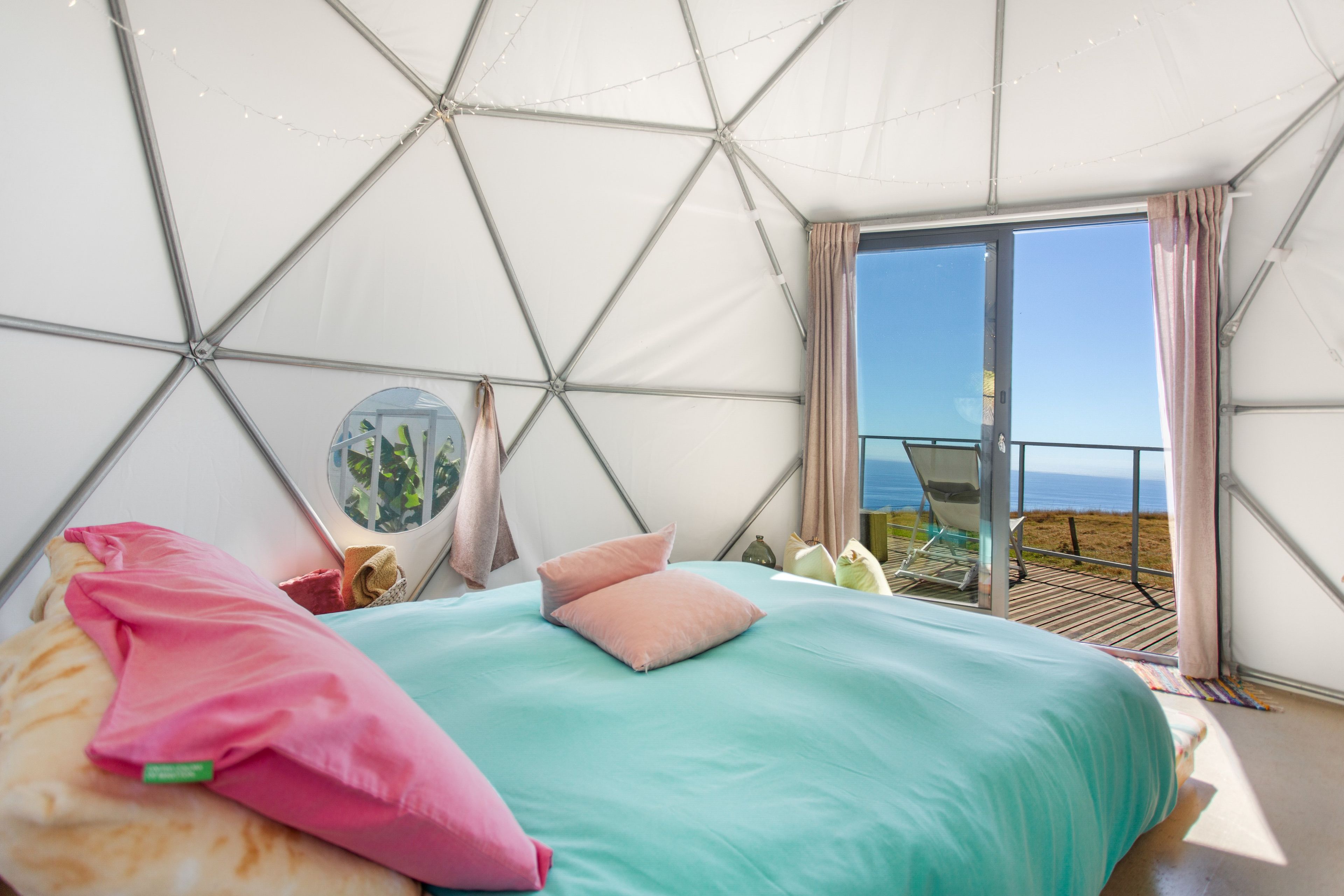 Quarto com cama, espelho redondo e vista para o mar.
