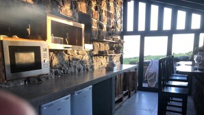 A kitchen with a stone wall, a microwave, a refrigerator, and a view of the outdoors. - Soulglamping – Rückzugsort – Natur – Meerblick – Sonne (Prazeres)