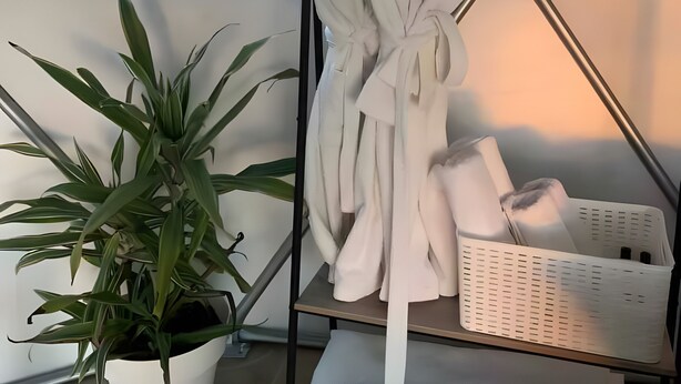 A room with a white wall, a round window, a white potted plant, a white robe hanging on a metal rack, and a white basket on a shelf. - Soulglamping – Rückzugsort – Natur – Meerblick – Sonne (Prazeres)