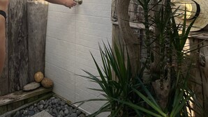 A woman in a black bikini opening a door to a room with a white tiled wall, a wooden tree trunk, and a straw hat on the floor. - Soulglamping – Rückzugsort – Natur – Meerblick – Sonne (Prazeres)