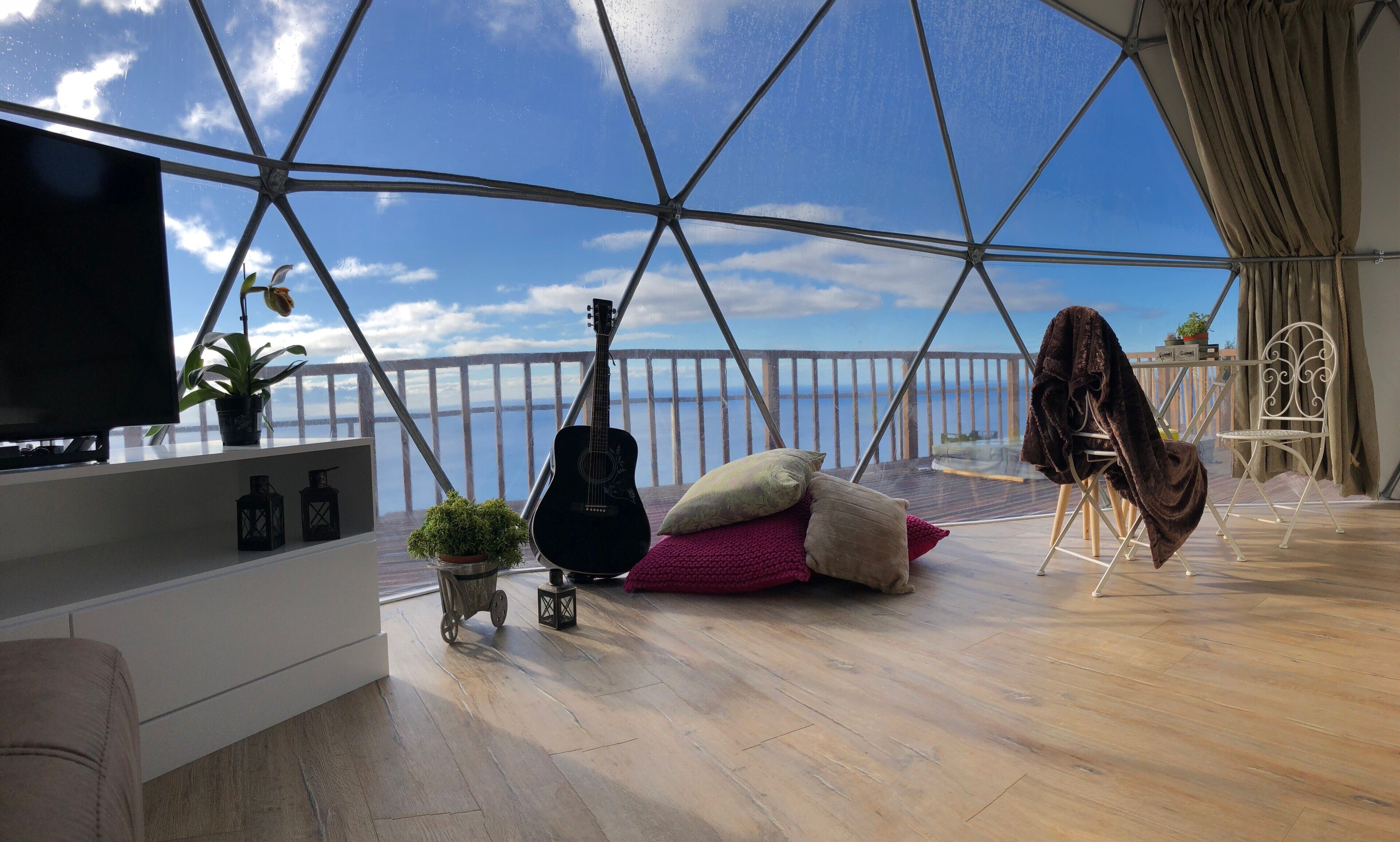 Una habitación con un ventanal grande, una guitarra, un televisor y una zona de estar acogedora con cojines.