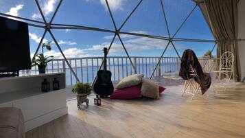 Una habitación con un ventanal grande, una guitarra, un televisor y una zona de estar acogedora con cojines.