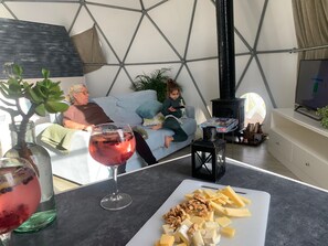 Ein Wohnzimmer mit einer Couch, einem Tisch mit Essen, einem Weinglas und einem Fernseher.