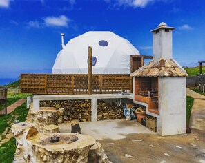 A dome-shaped building with a chimney, a wooden fence, and a fire pit area.