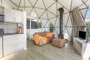 A modern interior with a geometric ceiling, a sofa set, a television, and a kitchen area.