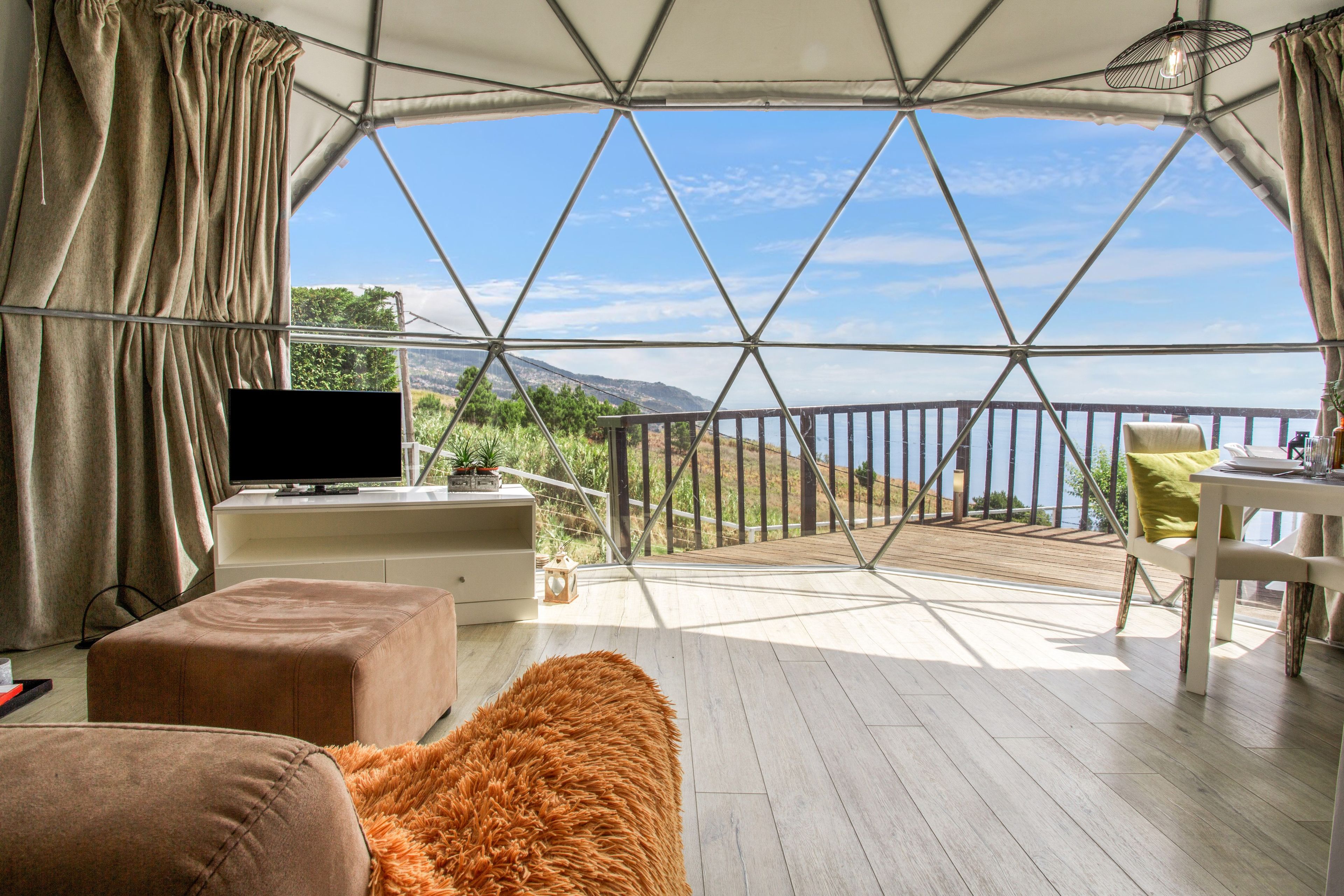 Una habitación con un ventanal grande, televisión, terraza de madera y un sofá.