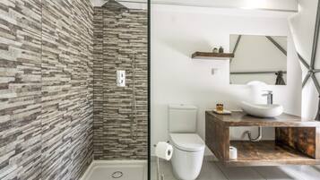Un baño moderno con pared de piedra, ducha envuelta en vidrio, inodoro blanco y tocador de madera con lavamanos.