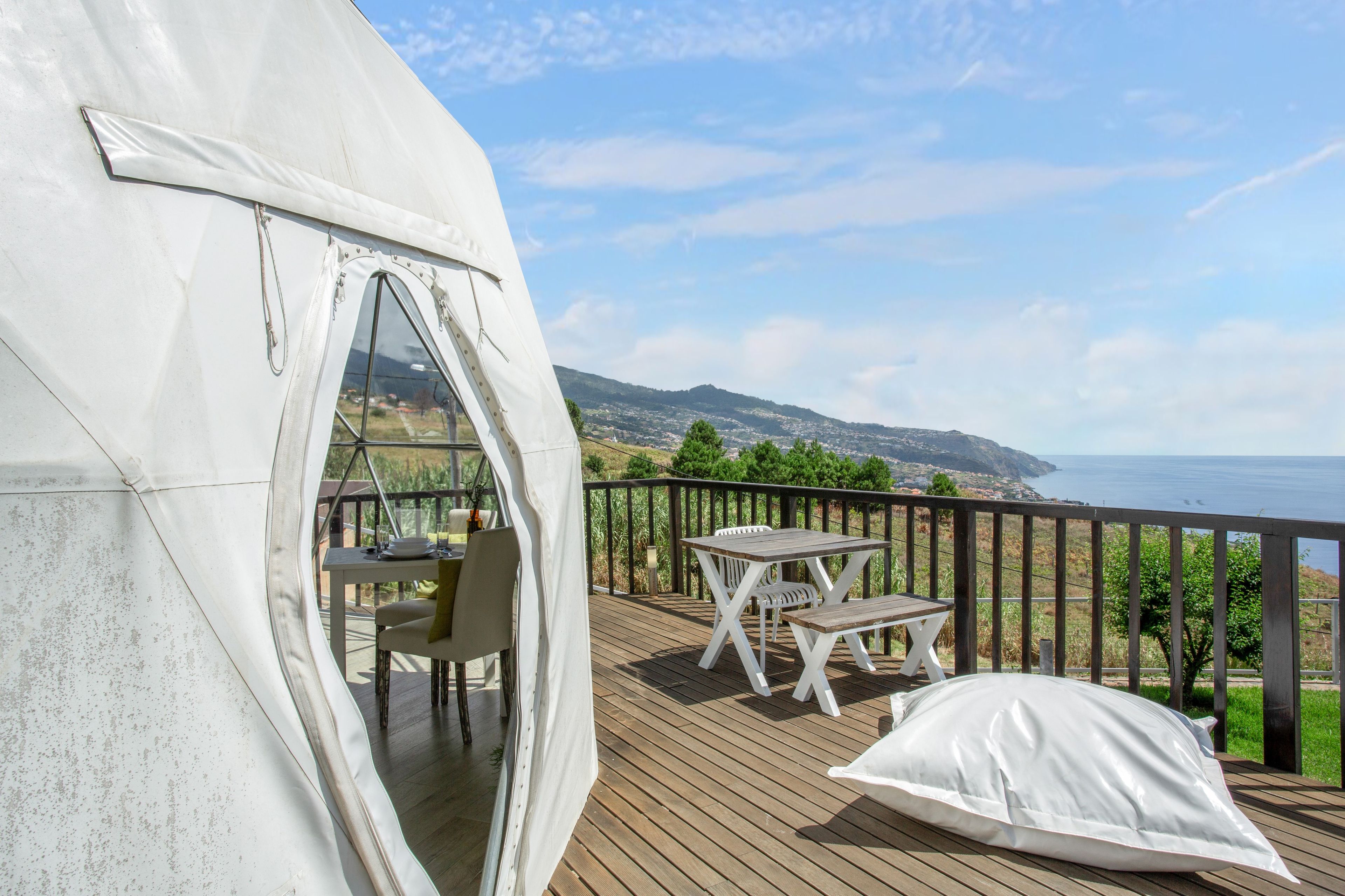 A tent with a table and chairs on a deck overlooking a coastal landscape.