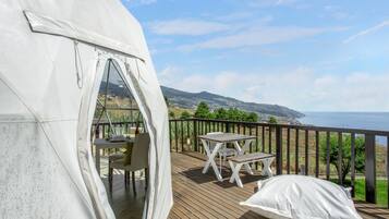 A tent with a table and chairs on a deck overlooking a coastal landscape.