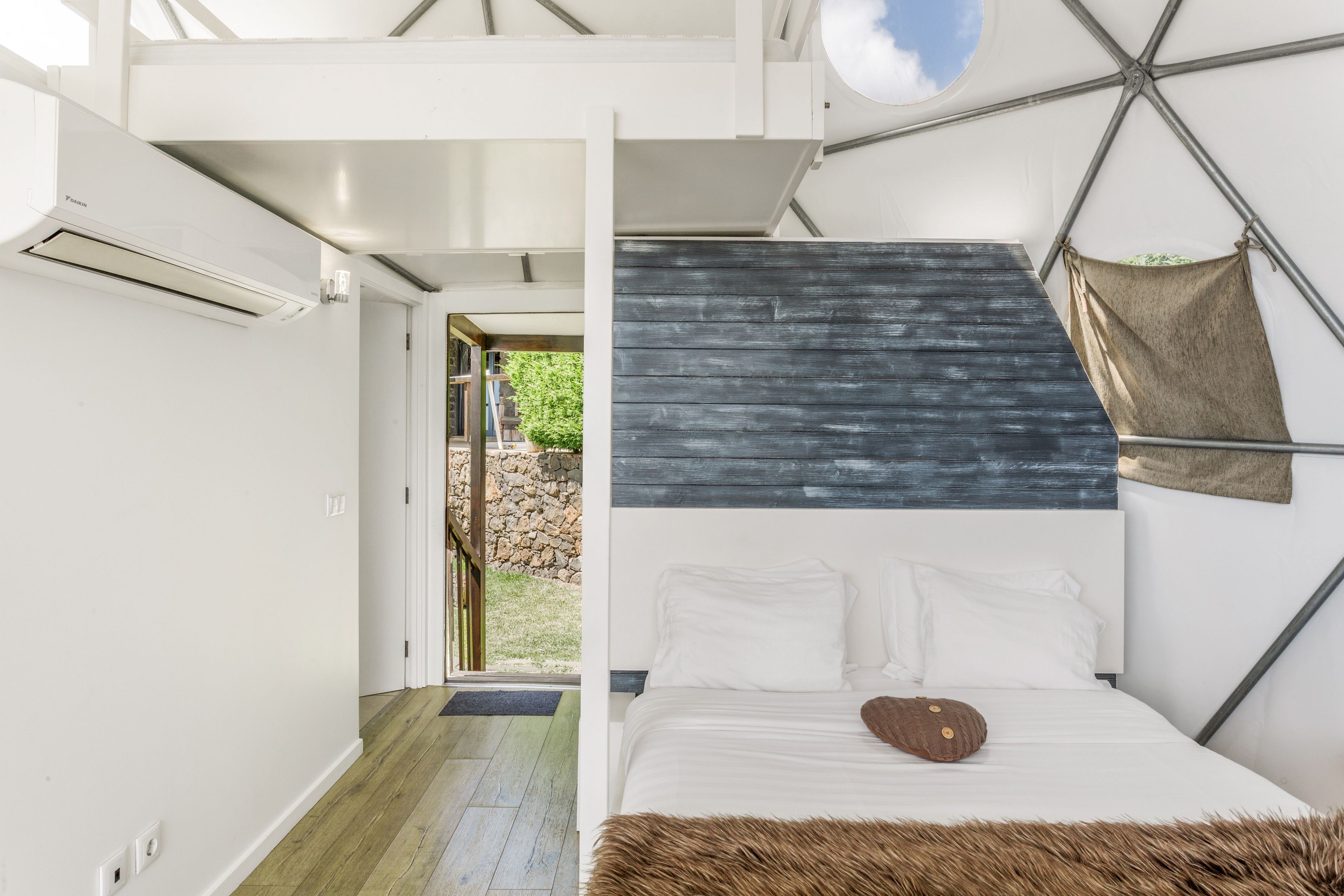 Ein modernes Schlafzimmer mit einem geometrischen Deckenmuster, einem Bett mit weißen Leinen und Blick ins Freie.