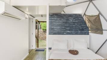 Ein modernes Schlafzimmer mit einem geometrischen Deckenmuster, einem Bett mit weißen Leinen und Blick ins Freie.