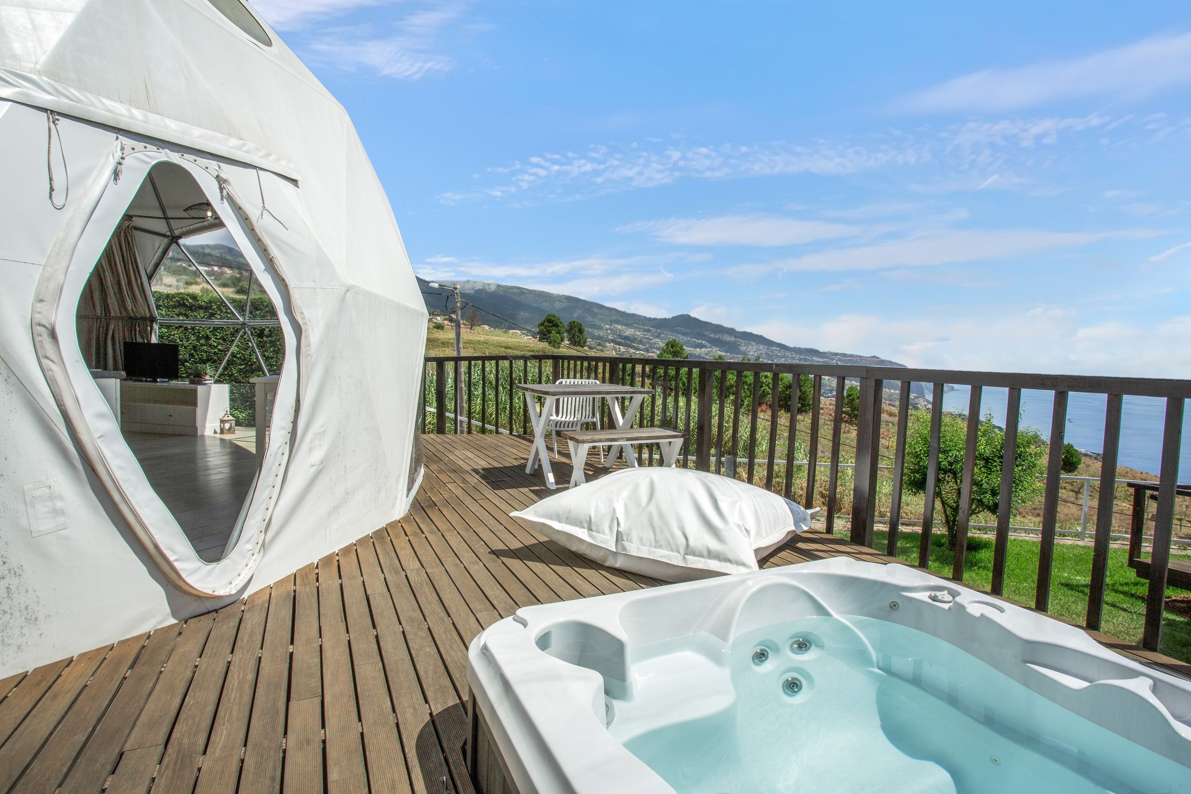 A wooden deck with a hot tub, a tent, and a table with chairs.