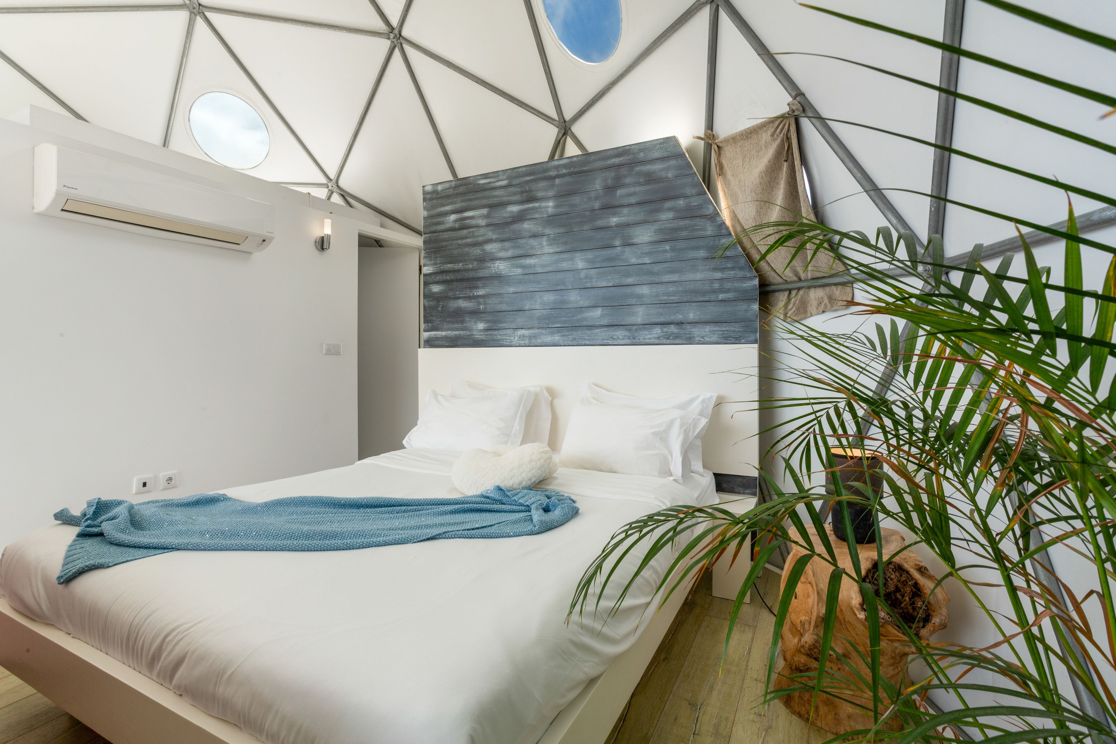 Un dormitorio moderno con cama, almohadas, una toalla azul y un ventanal grande.