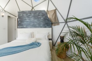 Ein Schlafzimmer mit einem Bett, Kissen, einer Decke, einer Wandleuchte und einer Pflanze.