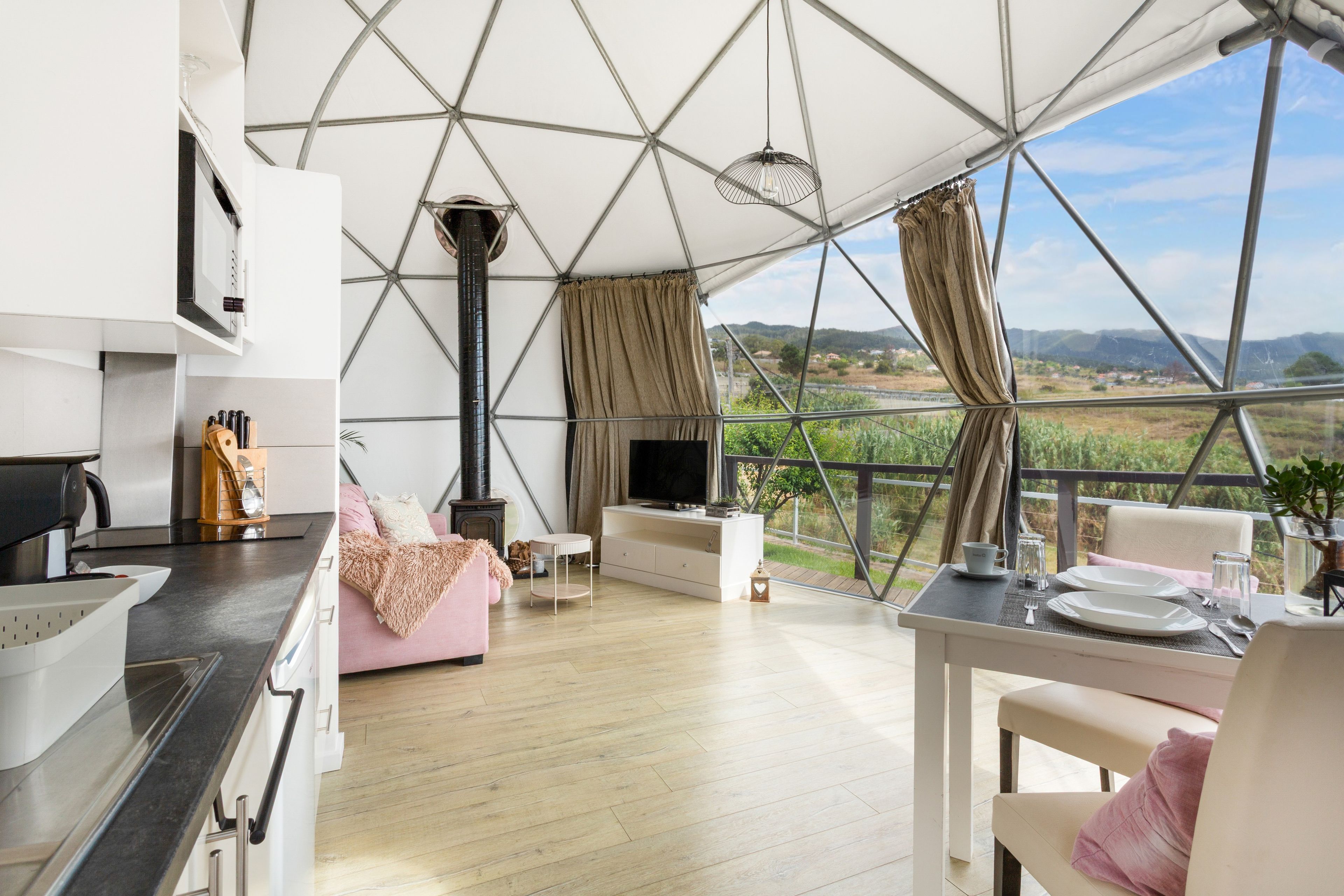 Un intérieur moderne comprenant une cuisine, un coin repas et un espace de vie, avec une grande fenêtre offrant une vue sur la campagne.