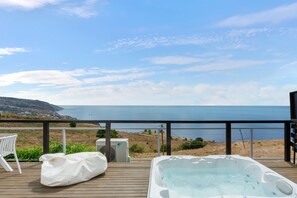 Ein Whirlpool auf einer Holzterrasse mit Blick auf das Meer und eine entfernte Stadt.