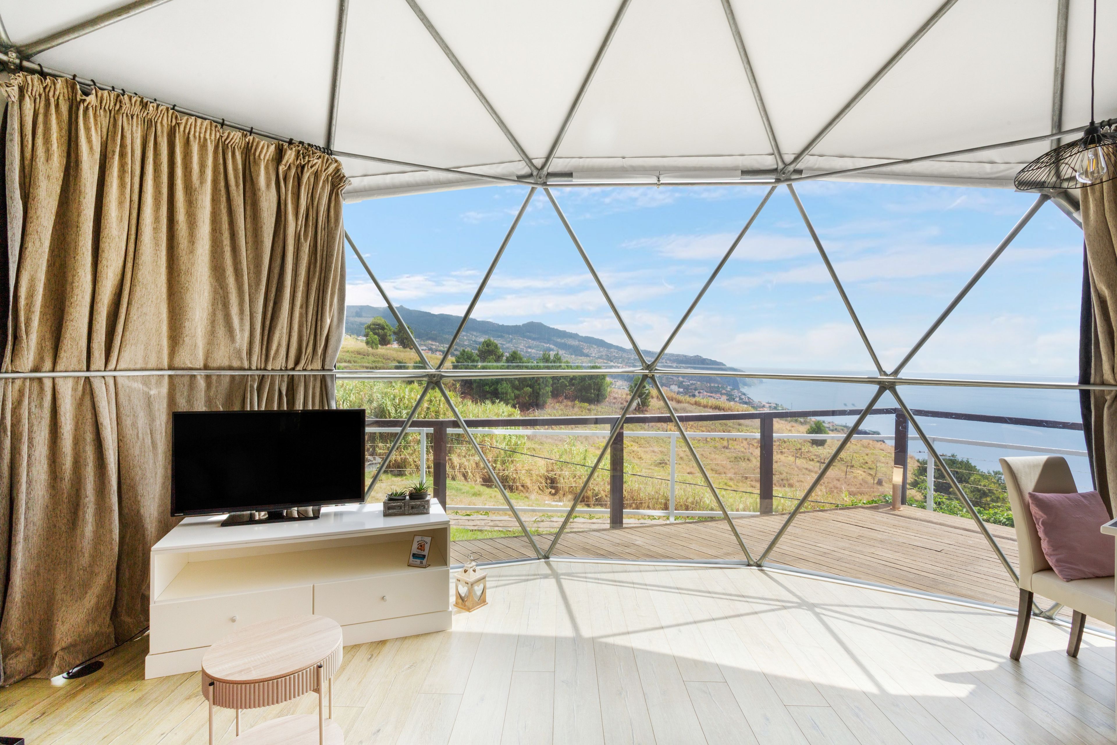 Una habitación con un ventanal grande, televisión, una mesita y una silla.